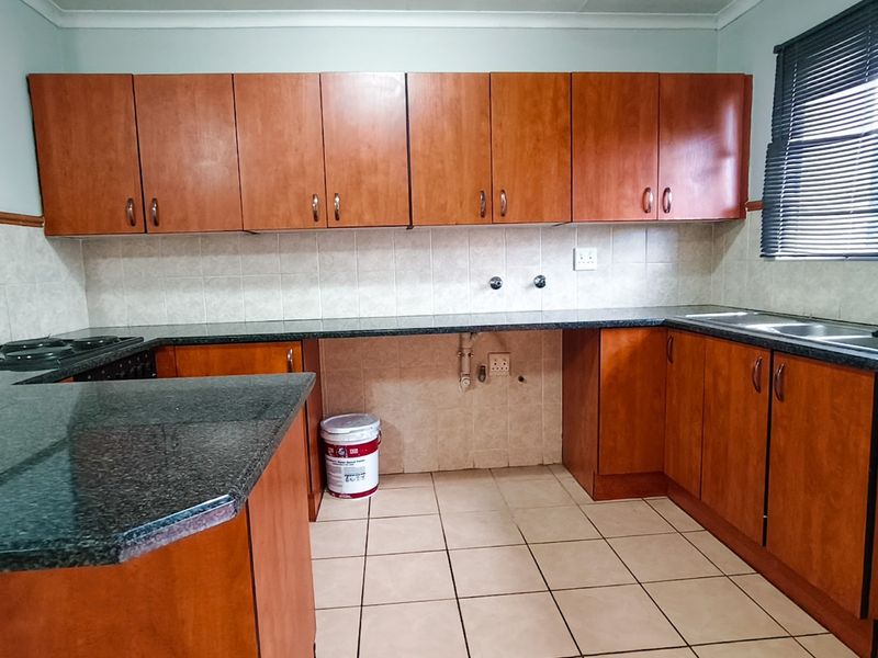 A functional kitchen featuring wood-finish cabinetry, granite countertops, tiled backsplash, and a double basin sink, offering a clean and practical workspace.