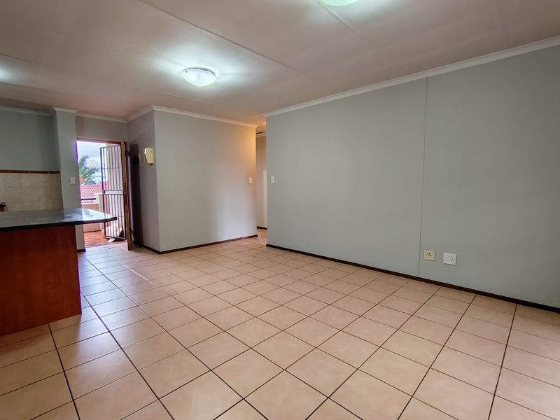 An open-plan living and kitchen area featuring neutral wall tones, ceramic tiled flooring, and direct access to an outdoor balcony through a security gate.