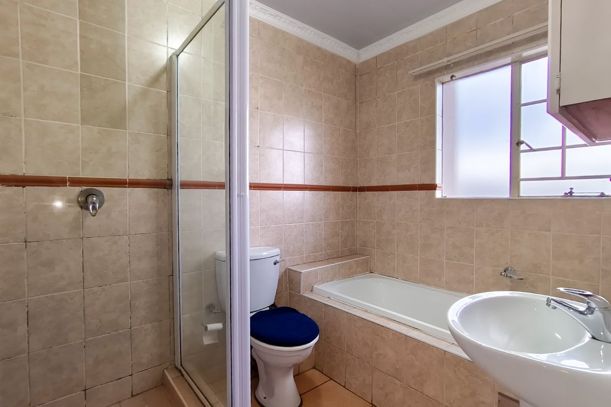 A functional bathroom featuring a shower enclosure, built-in bathtub, pedestal basin, and toilet with neutral tiled finishes throughout.