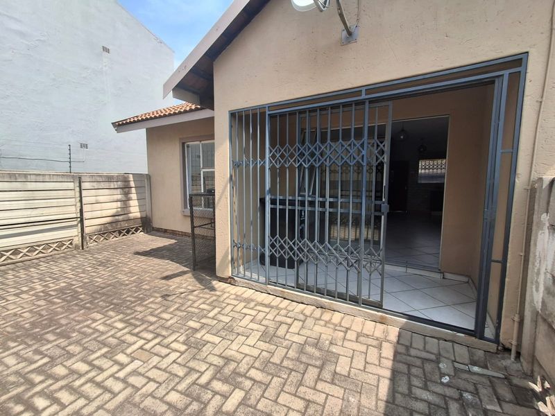 Rear exterior view of the townhouse featuring a paved patio area, security gate access, and boundary walling.