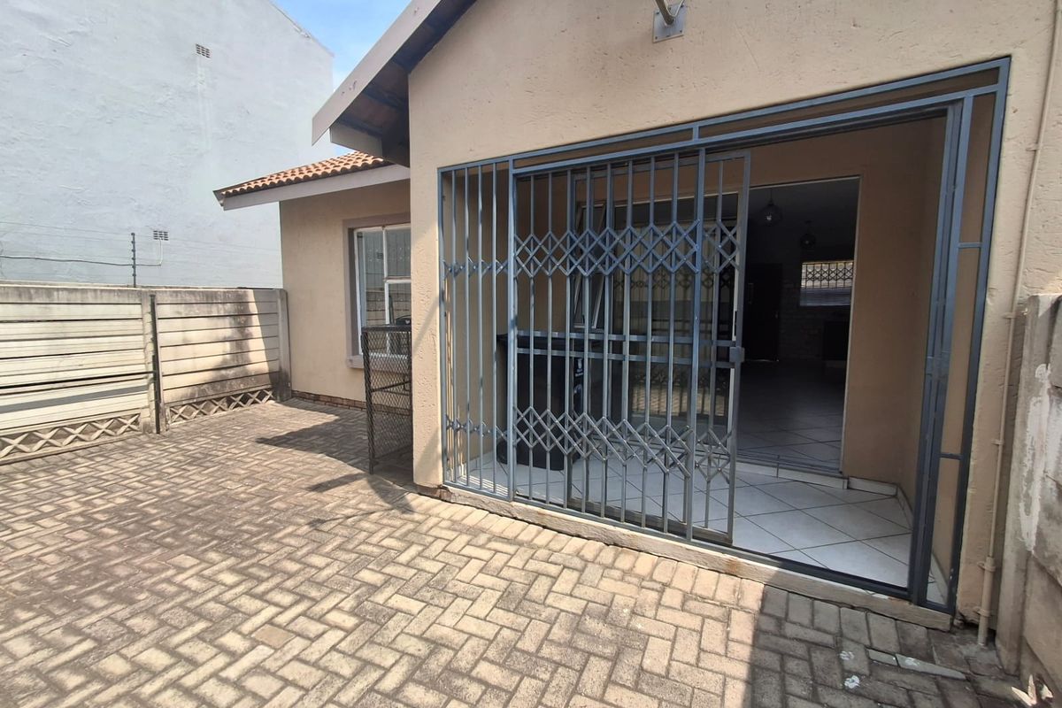 Rear exterior view of the townhouse featuring a paved patio area, security gate access, and boundary walling.