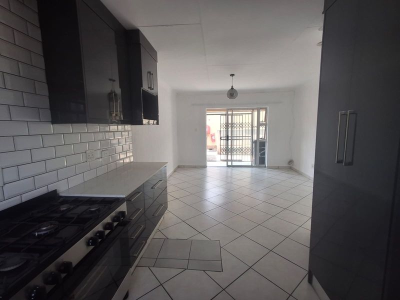 Open-plan kitchen and living area featuring modern dark cabinetry, subway tile backsplash, gas stove, and direct access to an outdoor space via sliding doors.