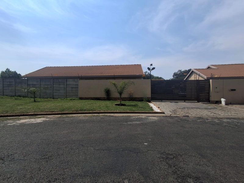 Front exterior view of the townhouse featuring a paved driveway, secure sliding gate, perimeter wall with electric fencing, and a well-maintained lawn.