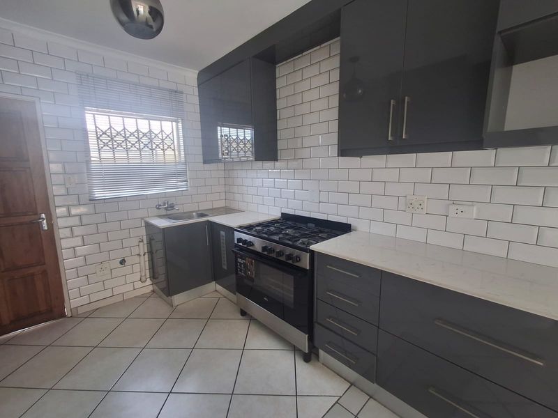 Modern kitchen featuring dark grey cabinetry, white subway tile backsplash, stone countertops, and a stainless steel gas stove.