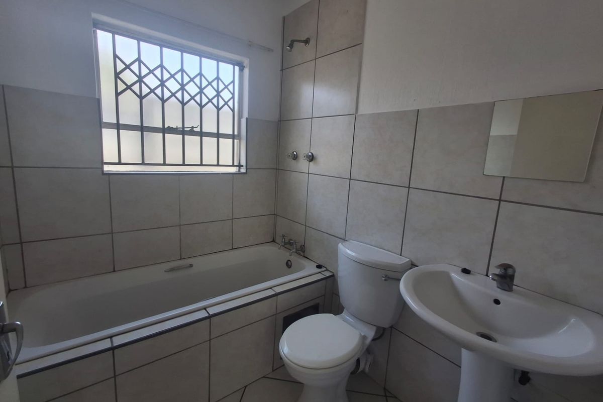 A functional bathroom featuring a bathtub, pedestal basin, and toilet with neutral wall and floor tiling.