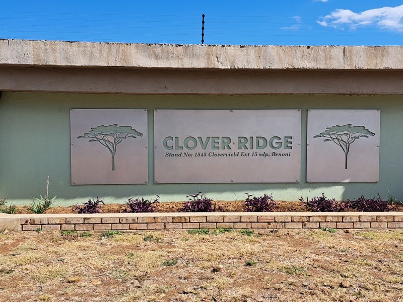 The entrance signage and boundary wall for Clover Ridge complex, featuring integrated electric fencing and a brick planter bed.