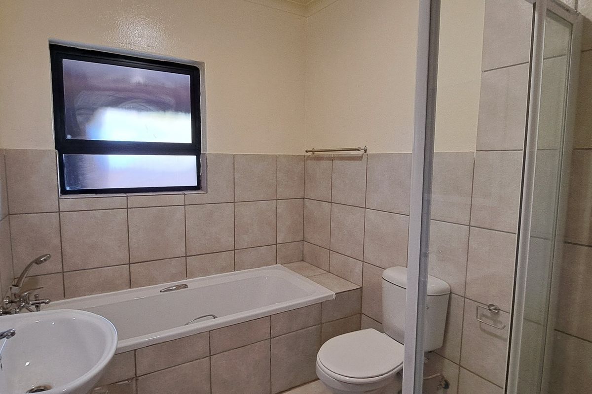 A functional bathroom featuring a bathtub, separate shower enclosure, pedestal basin, and neutral wall tiling.