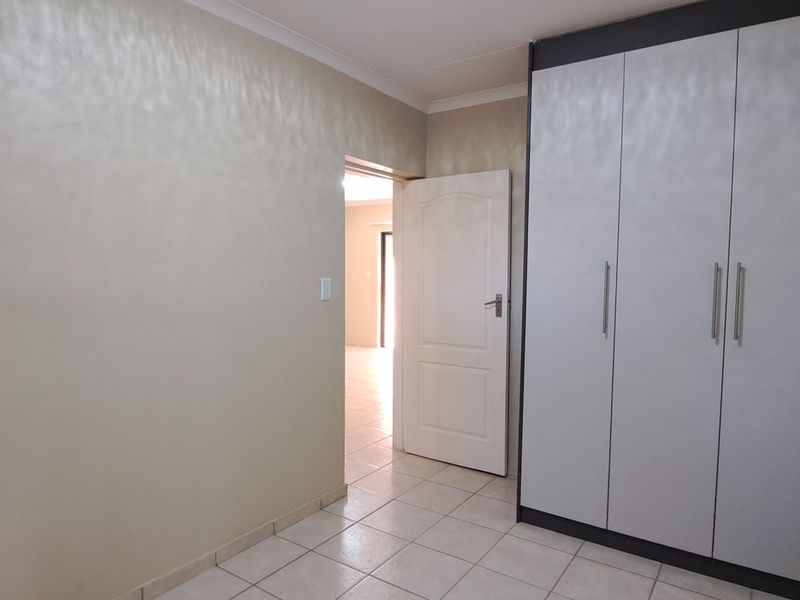 A clean, empty bedroom featuring neutral tiled flooring, a modern built-in wardrobe, and a doorway leading to an adjacent living space.