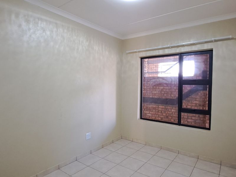 A clean, empty bedroom featuring neutral tiled flooring, coving, and a dark aluminium-framed window with an installed curtain rail.