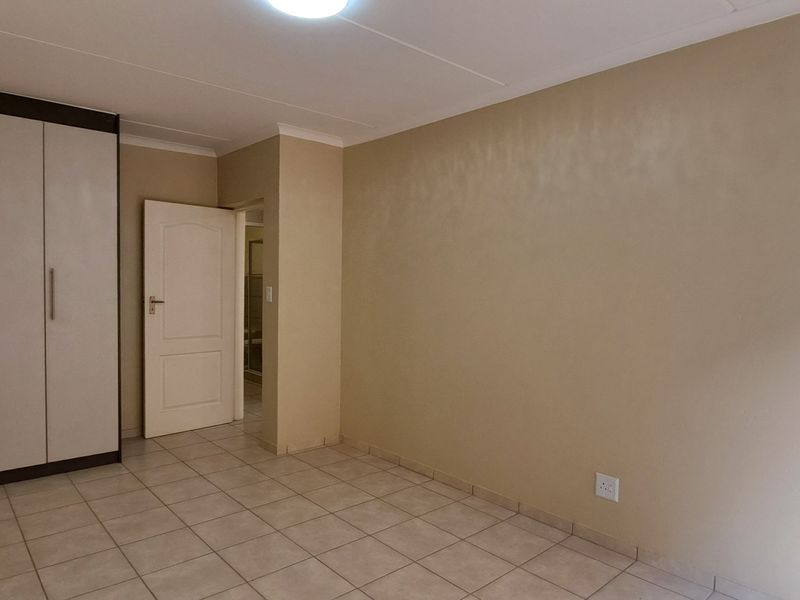 A clean, empty bedroom featuring neutral tiled flooring, a built-in wardrobe, and a simple ceiling light fixture.