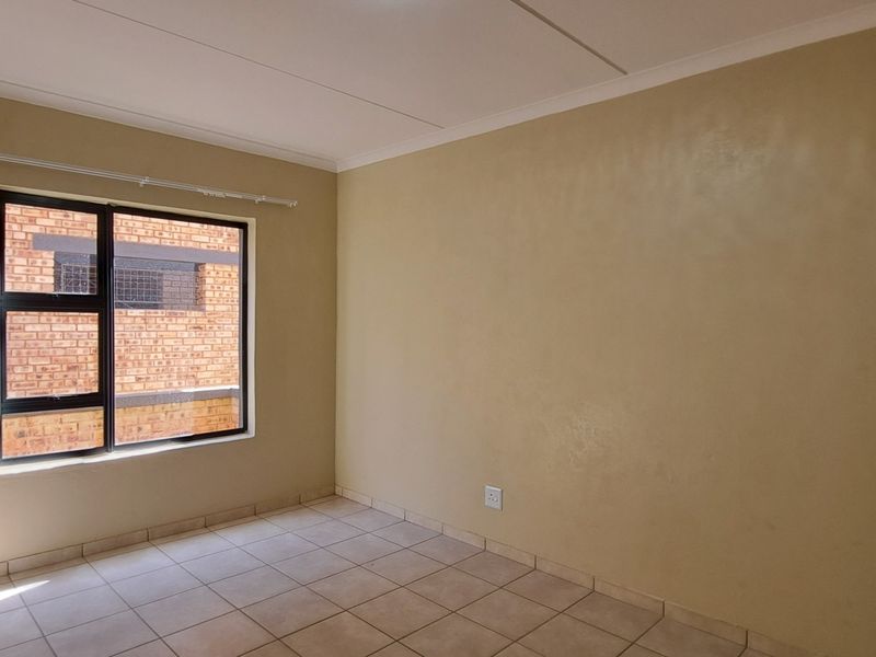 A bright, empty bedroom featuring neutral wall paint, tiled flooring, and an aluminium-framed window with a fitted curtain rail.