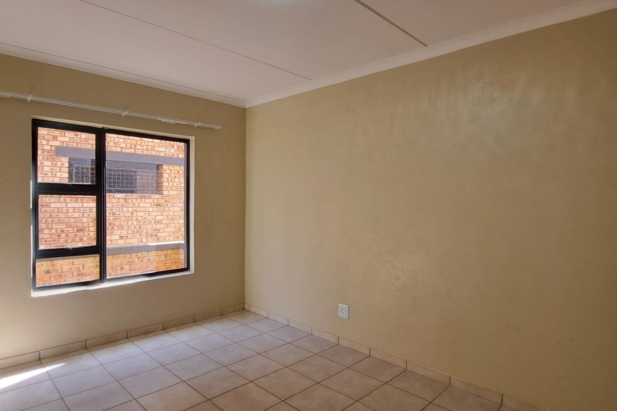 A bright, empty bedroom featuring neutral wall paint, tiled flooring, and an aluminium-framed window with a fitted curtain rail.