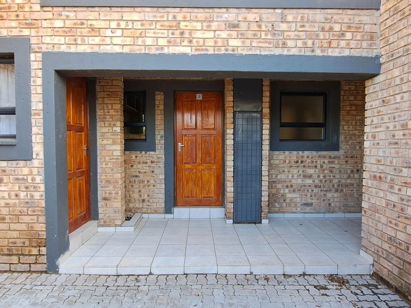 Front entrance area of the apartment featuring a face brick facade, tiled patio, and timber door with aluminium window frames.