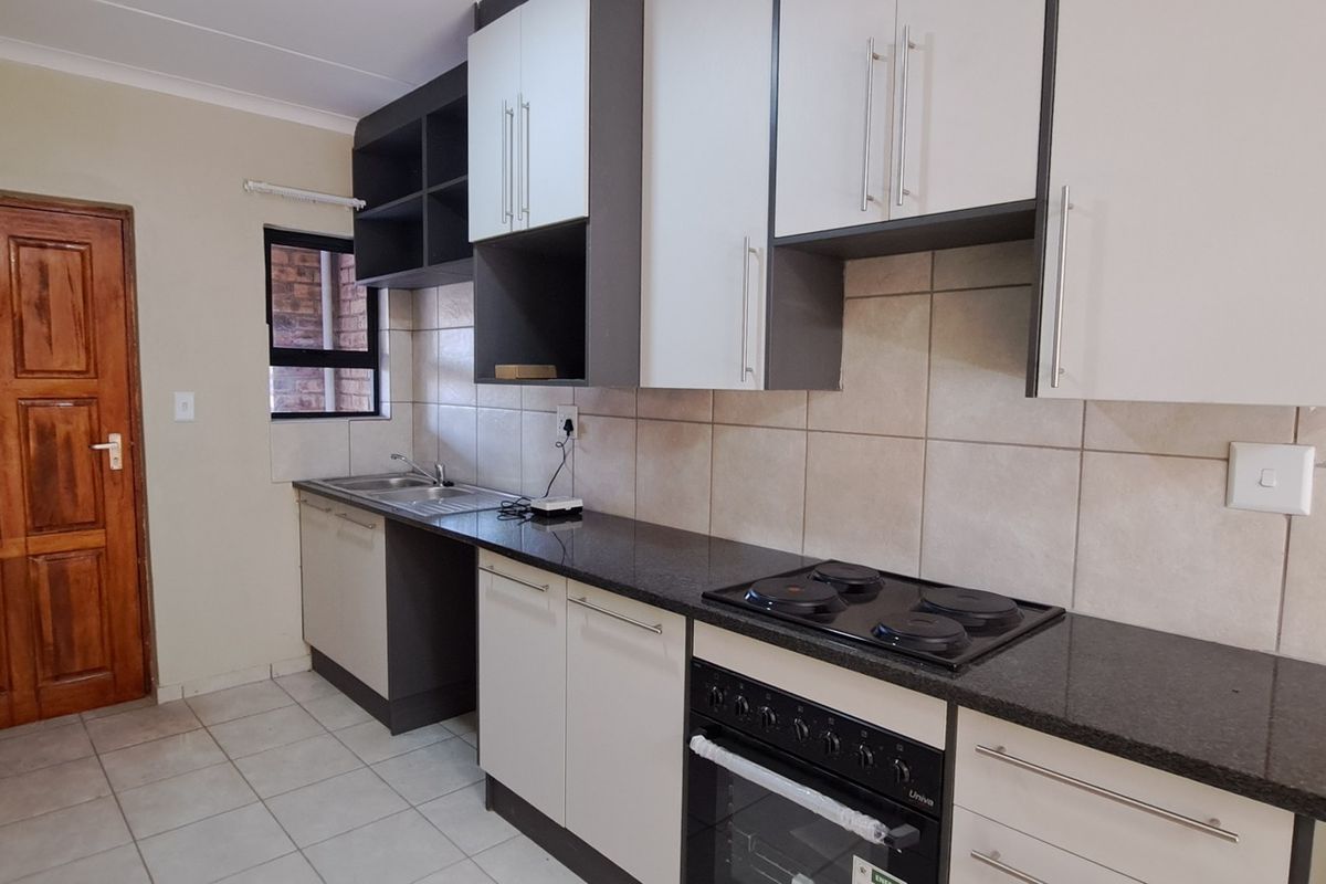 A functional kitchen featuring modern two-tone cabinetry, granite countertops, a built-in oven with electric hob, and tiled finishes throughout.