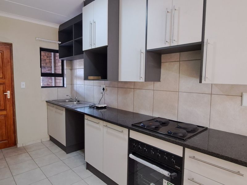 A functional kitchen featuring modern two-tone cabinetry, granite countertops, a built-in oven with electric hob, and tiled finishes throughout.