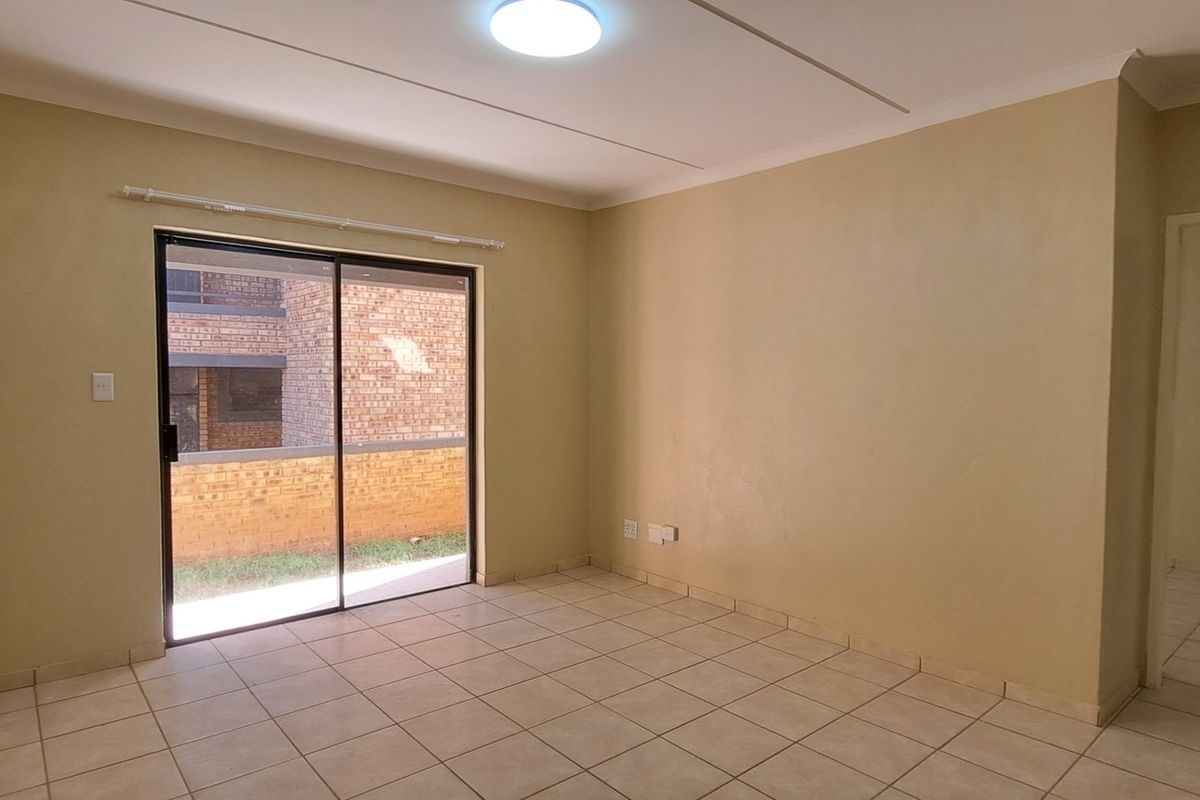 An empty living room featuring neutral tiled flooring, a sliding glass door leading to an outdoor area, and a simple ceiling light fixture.