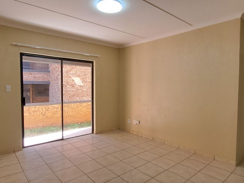 An empty living room featuring neutral tiled flooring, a sliding glass door leading to an outdoor area, and a simple ceiling light fixture.