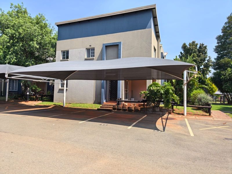 Front exterior view of the townhouse featuring a covered carport, paved driveway, and a secure entrance with stairs.