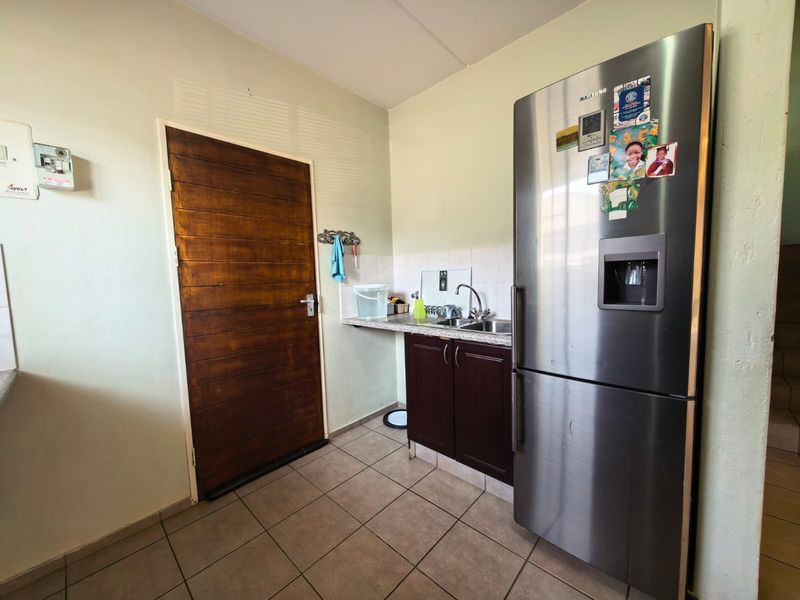 A functional scullery area featuring built-in cabinetry, a stainless steel sink, tiled splashback, and tiled flooring, providing practical utility space.