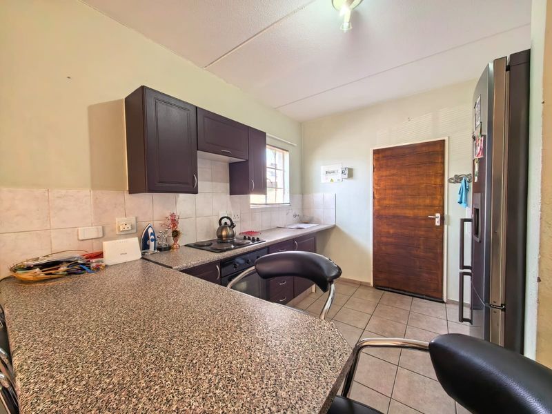 A functional kitchen featuring dark wood cabinetry, granite countertops, tiled backsplash, and tiled flooring, providing a practical workspace with direct access to an exterior door.