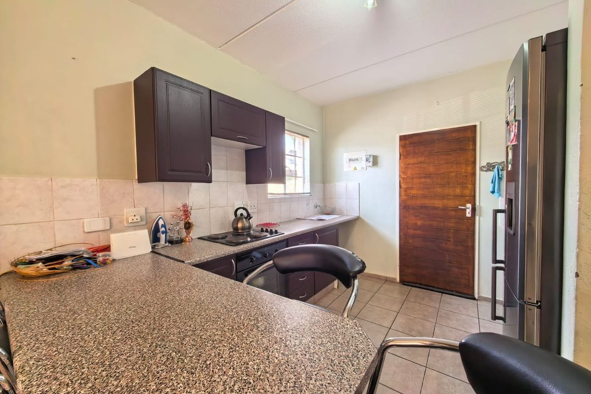 A functional kitchen featuring dark wood cabinetry, granite countertops, tiled backsplash, and tiled flooring, providing a practical workspace with direct access to an exterior door.