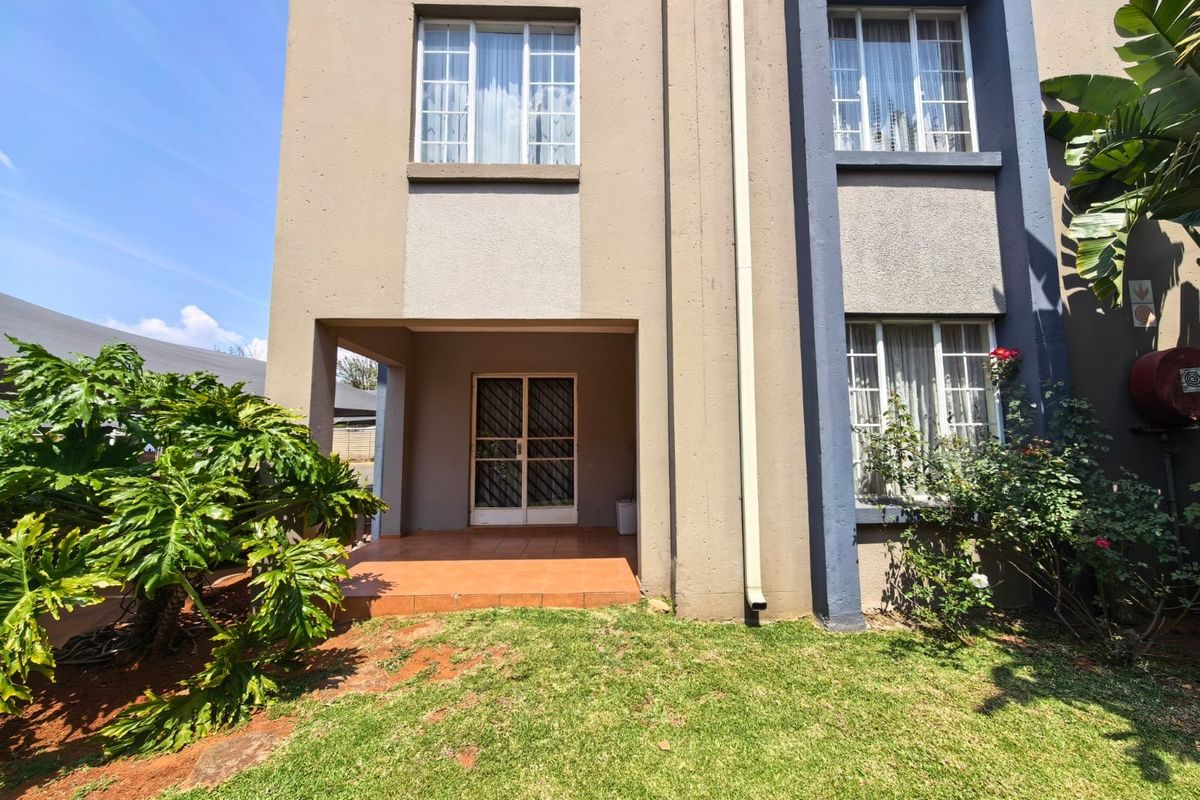 Rear view of the townhouse featuring a tiled patio area, security gate, and a small private garden space.
