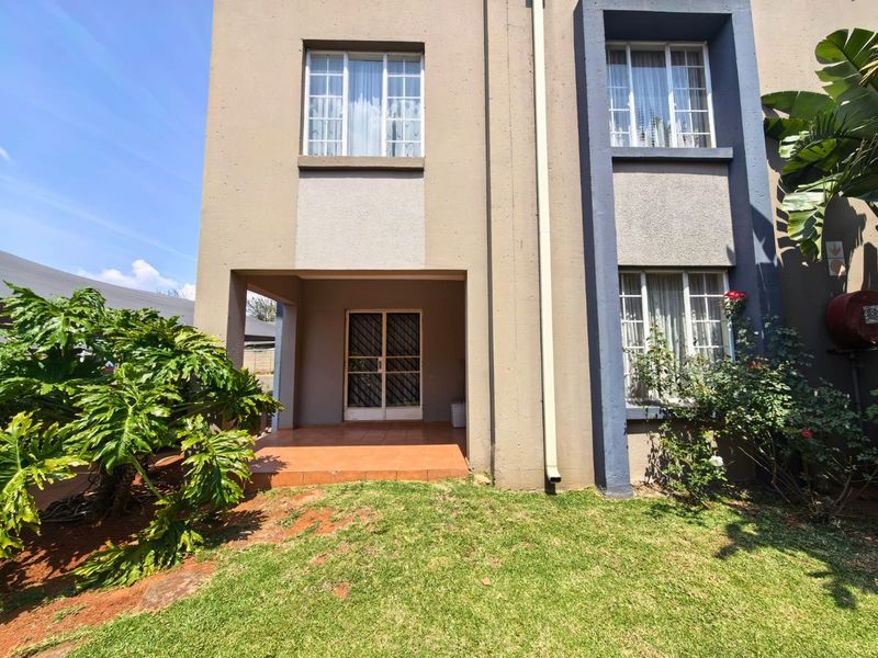 Rear view of the townhouse featuring a tiled patio area, security gate, and a small private garden space.