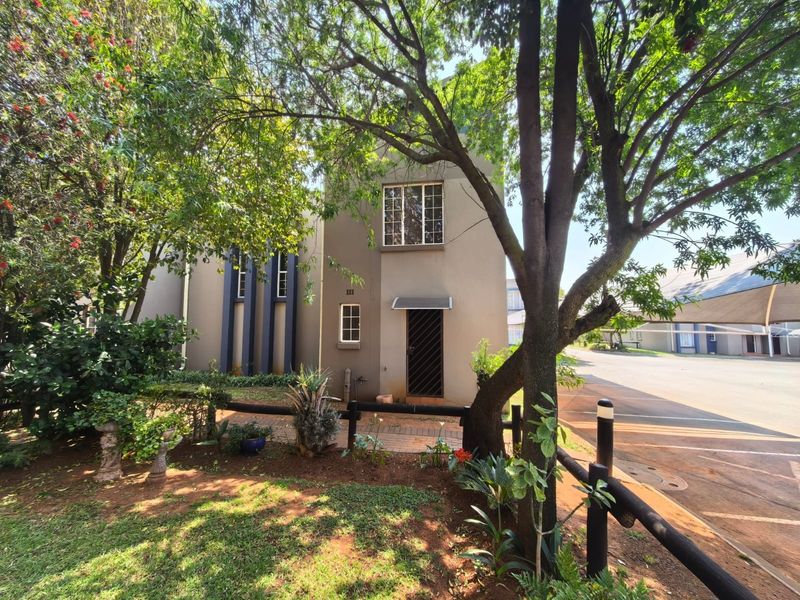 Front elevation of the townhouse featuring a paved entrance path, security gate, and established garden surroundings.