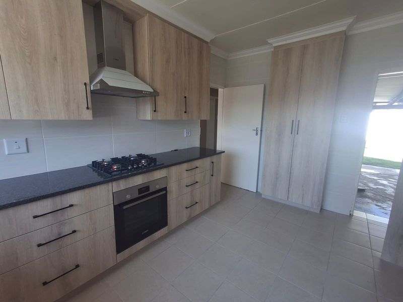Modern kitchen featuring light wood-grain cabinetry, stone countertops, built-in gas hob, electric oven, extractor fan, and neutral tiled flooring.