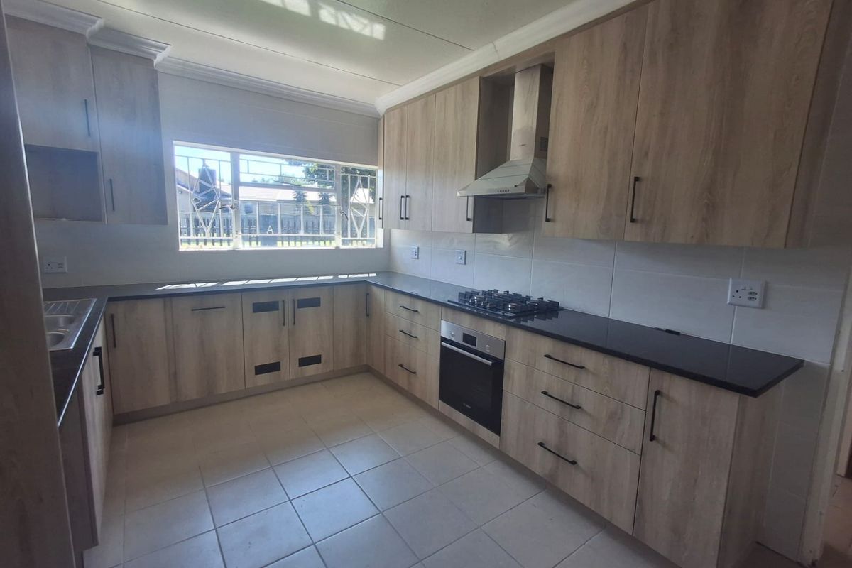 A modern, clean kitchen featuring light wood-grain cabinetry, dark stone countertops, built-in oven, gas hob, and an extractor fan with neutral tiled flooring.