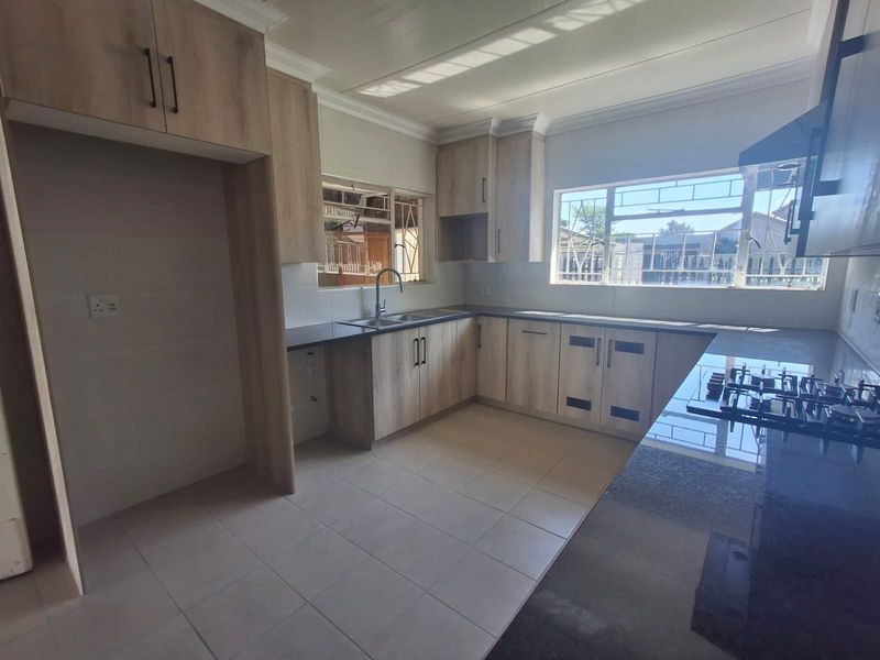 A clean, modern kitchen featuring light wood-finish cabinetry, dark countertops, a gas hob, and tiled flooring, offering a functional and well-lit workspace.