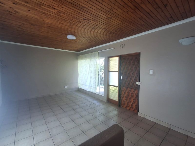 An empty living room featuring a timber tongue and groove ceiling, ceramic floor tiles, and a sliding glass door with an integrated security gate.