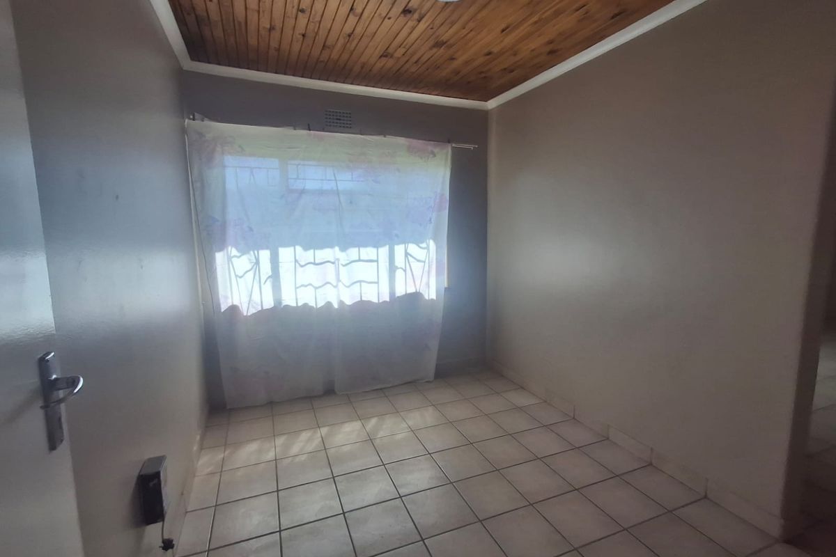 An empty bedroom featuring ceramic floor tiles and a wooden tongue and groove ceiling with a window fitted with security burglar bars.