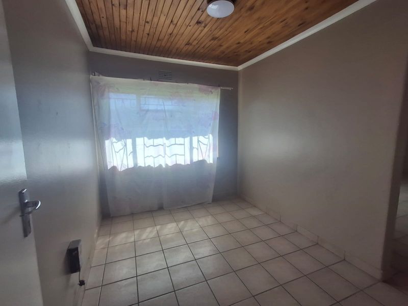 An empty bedroom featuring ceramic floor tiles and a wooden tongue and groove ceiling with a window fitted with security burglar bars.
