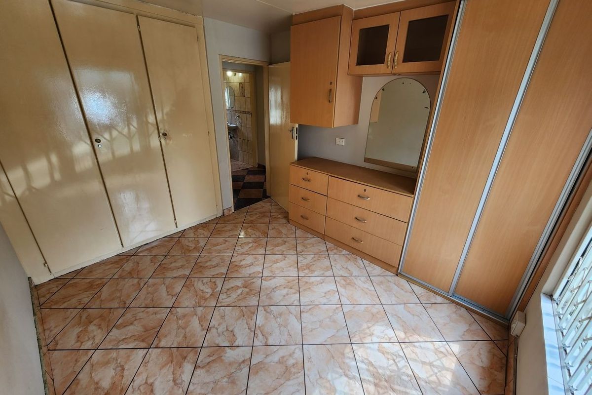A bedroom featuring built-in cupboards, a vanity unit, and tiled flooring, offering a functional space with potential for modern updates.