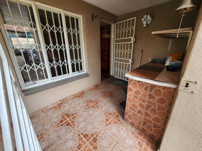 Covered patio area featuring tiled flooring, a built-in counter, and security gates on windows and doors.