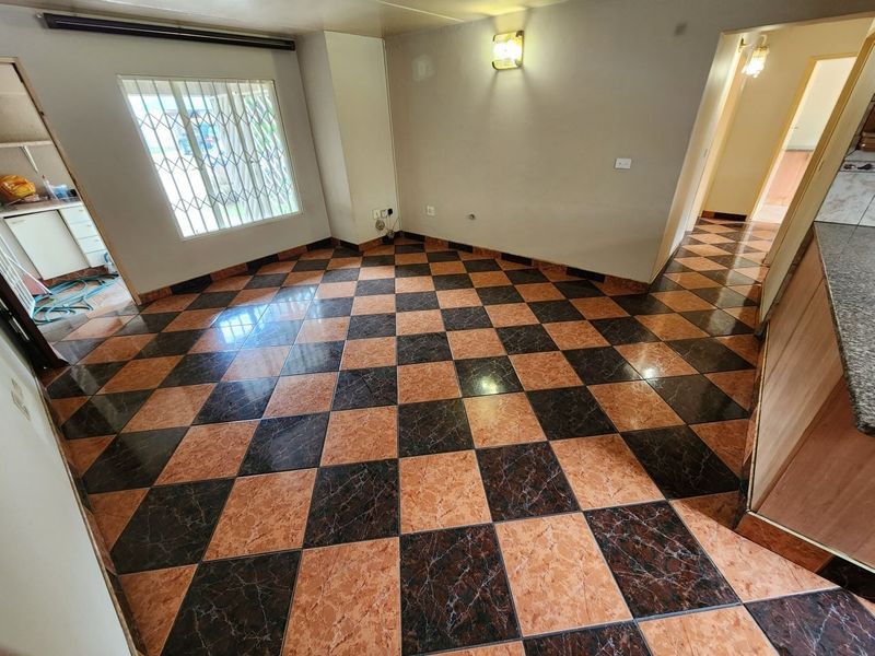 An empty living area featuring distinctive checkered ceramic floor tiles, a window with security bars, and neutral wall finishes.