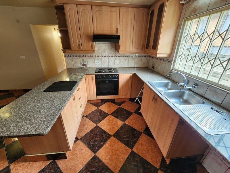 A functional kitchen featuring wooden cabinetry, granite countertops, a double basin sink, and built-in cooking appliances with a tiled backsplash.