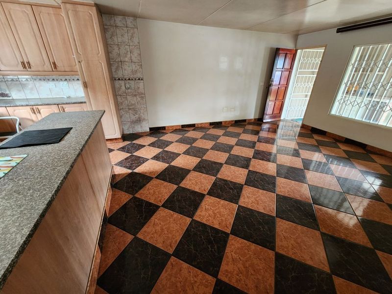 Open plan living area featuring tiled flooring, kitchen cabinetry with granite countertops, and secure access points with security gates and window bars.
