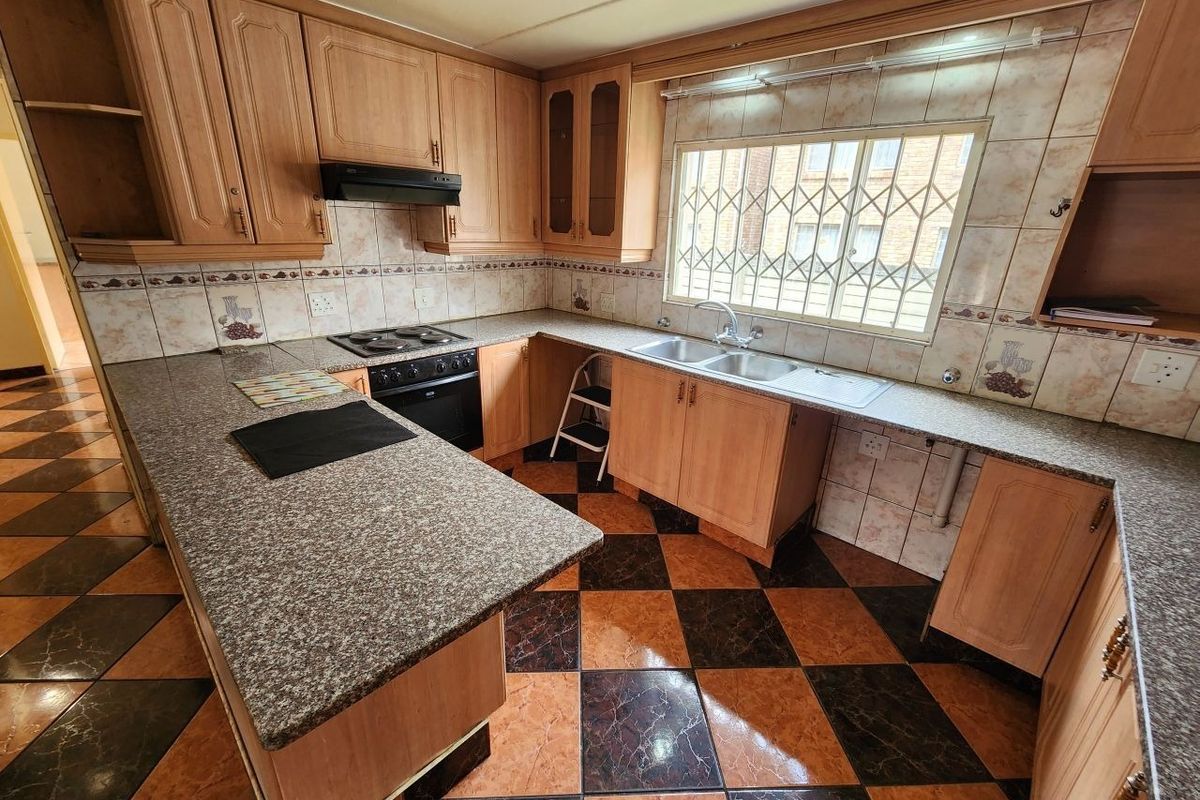 A functional kitchen featuring wooden cabinetry, granite countertops, a double basin sink, and integrated appliances, with a classic tiled backsplash and flooring.