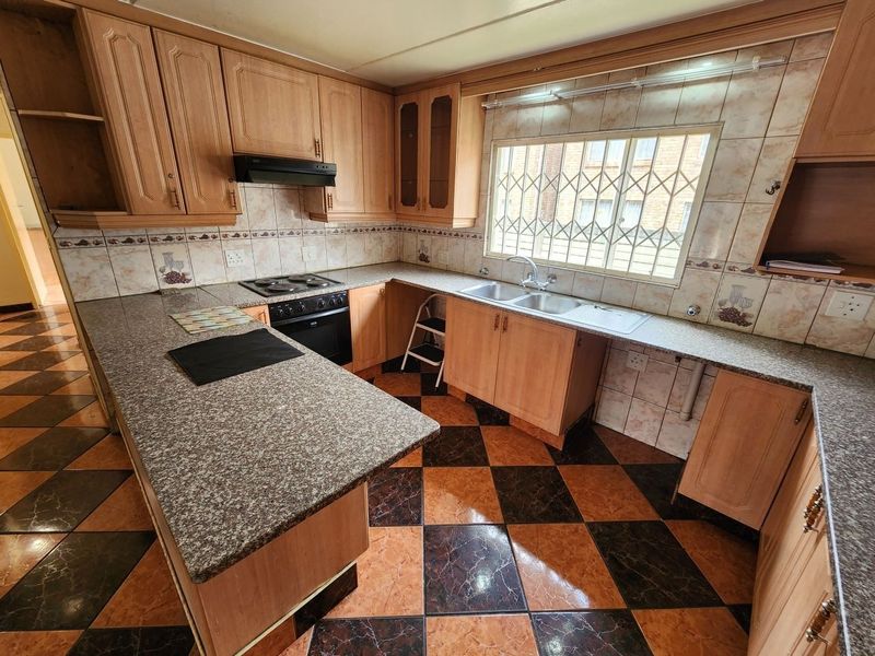 A functional kitchen featuring wooden cabinetry, granite countertops, a double basin sink, and integrated appliances, with a classic tiled backsplash and flooring.