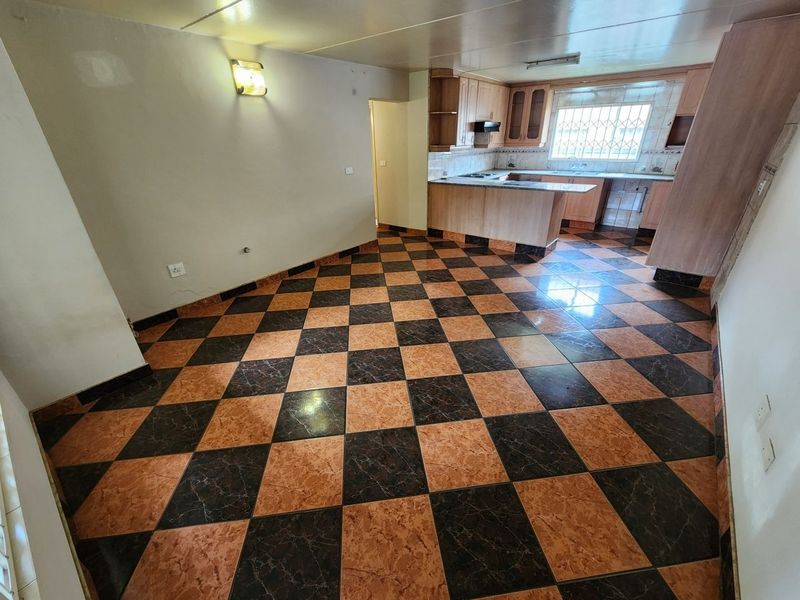 Open-plan living and kitchen area featuring checkered tile flooring, built-in wooden cabinetry, and a window with security bars.