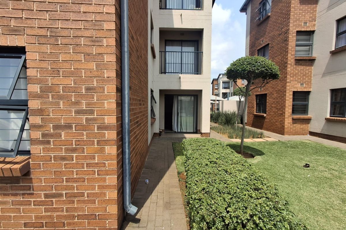 Exterior view of the apartment complex featuring face brick facades, paved walkways, and well-maintained communal garden areas with balcony access.