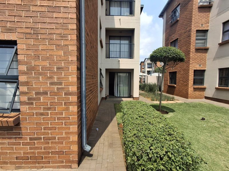 Exterior view of the apartment complex featuring face brick facades, paved walkways, and well-maintained communal garden areas with balcony access.