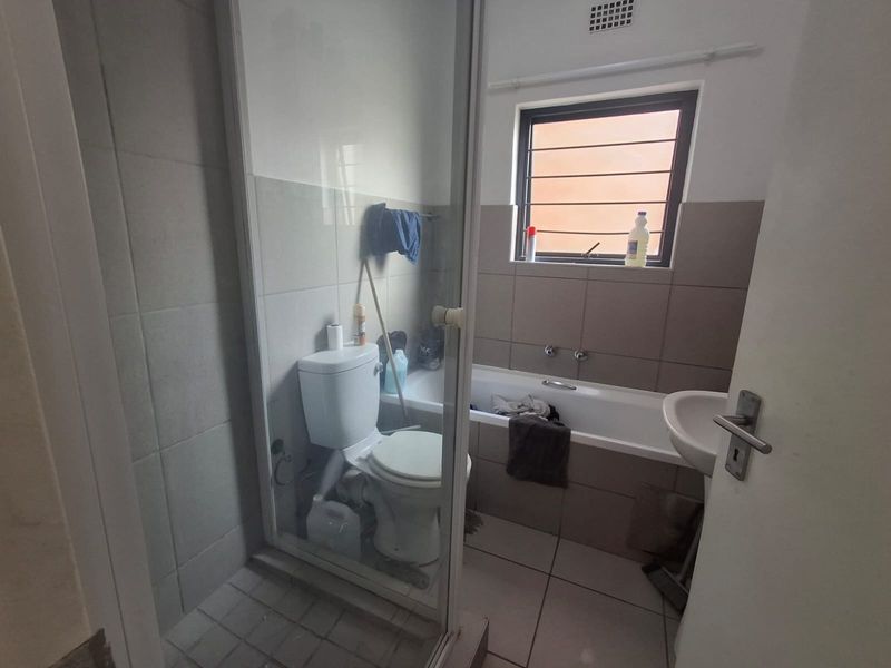 A functional bathroom featuring a shower enclosure, bathtub, pedestal basin, and toilet, finished with neutral wall and floor tiling.