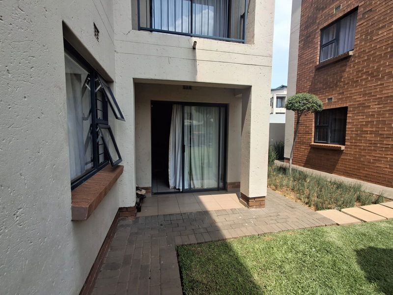 A ground floor patio area featuring paved flooring and a sliding glass door entrance, adjacent to a small garden space.