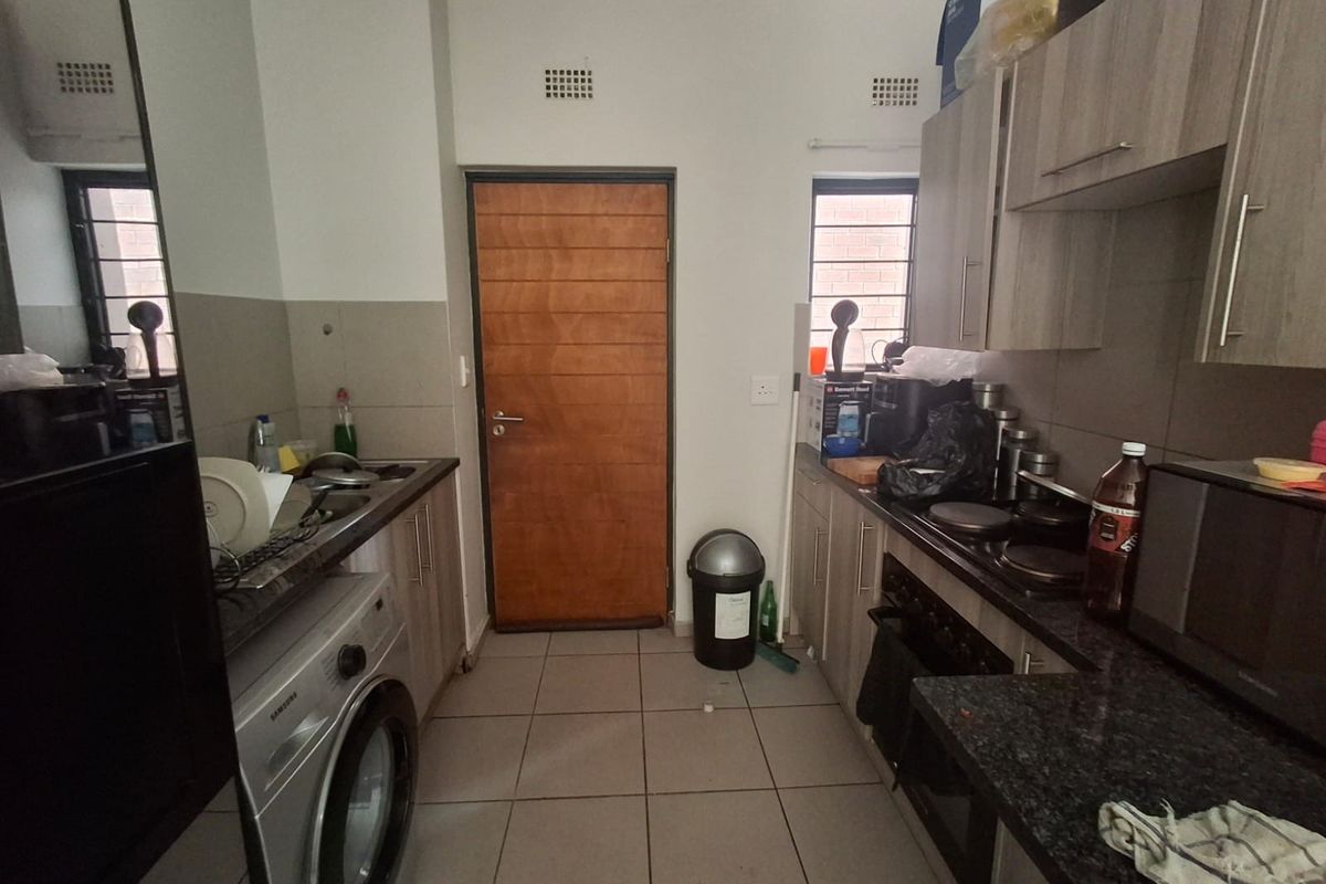A functional kitchen featuring built-in cabinetry, granite countertops, an integrated oven and hob, and tiled flooring with direct access to an exterior door.