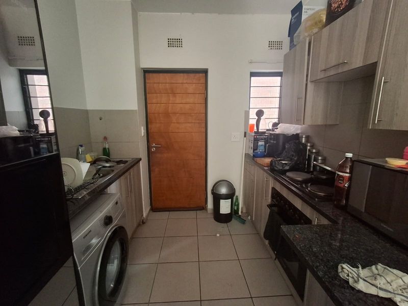 A functional kitchen featuring built-in cabinetry, granite countertops, an integrated oven and hob, and tiled flooring with direct access to an exterior door.