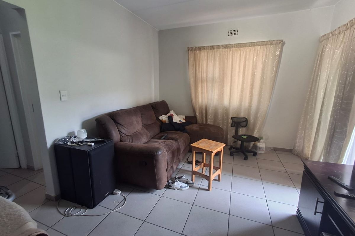 A living room area featuring neutral tiled flooring and a ventilation grille, providing a functional space ready for modernization.
