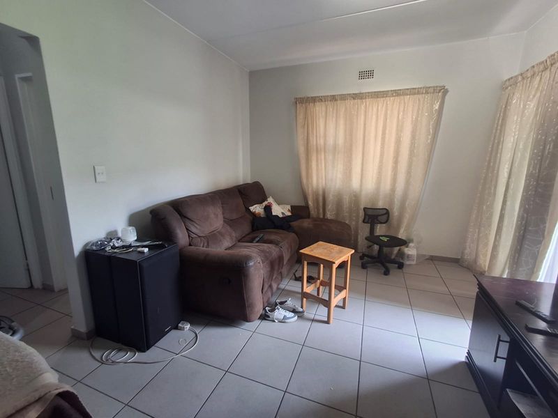 A living room area featuring neutral tiled flooring and a ventilation grille, providing a functional space ready for modernization.
